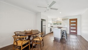 A modern kitchen with white cabinets, a stainless steel refrigerator, and a wooden dining table with chairs. - Moonee Stayz - Bungalow 5 (Moonee Beach)