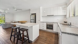 A modern kitchen with white cabinetry, a built-in oven, and a large island with stools. - Moonee Stayz - Bungalow 5 (Moonee Beach)
