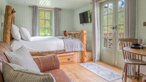 A cozy bedroom with a large bed, wooden headboard, and a TV mounted on the wall. - Juniper Lodge, Shepherd's Hut  for 2 in the Lake District with exclusive hot tub (Coniston)