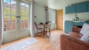 A cozy room with a wooden floor, a dining table with chairs, a sofa, and a kitchen area with teal cabinets. - Juniper Lodge, Shepherd's Hut  for 2 in the Lake District with exclusive hot tub (Coniston)