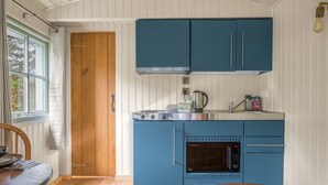 A compact kitchen with blue cabinets, a stove, and a sink. - Bluebell Lodge, Lake District Shepherd's Hut for 2 with hot tub (Coniston)