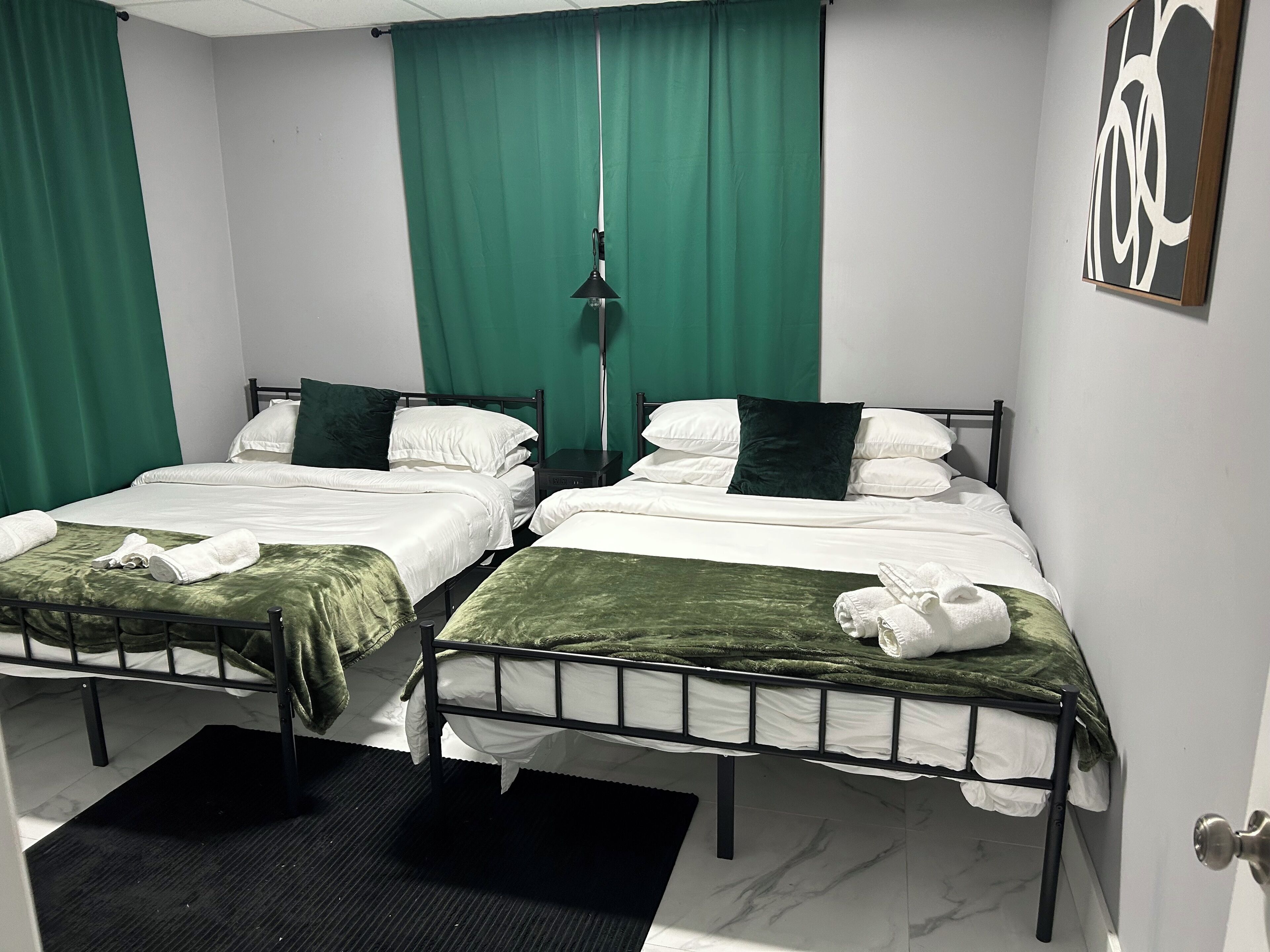 Une chambre d’hôtel avec deux lits, des rideaux verts, un tableau au mur et une porte dotée d’une poignée ronde.