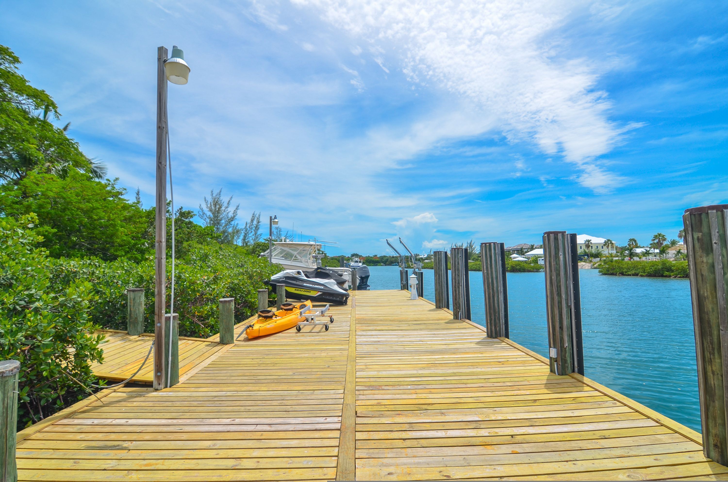 Un muelle de madera que llega al agua, con kayaks y un jet ski amarrados al costado.