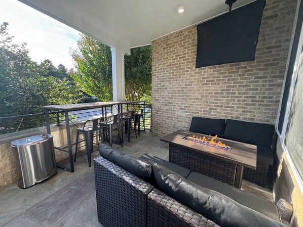 An outdoor patio with a brick wall, a dining table with chairs, a sofa, and a fire feature.