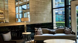 A modern living room with a sofa, armchair, and coffee table, featuring a large mirror and a view of the outdoors.