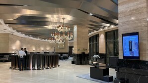 A modern hotel lobby with a reception desk, a large chandelier, and a digital display.