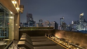 A rooftop terrace with a city skyline view, outdoor seating, and a glass enclosure.