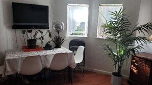 A dining area with a table set for two, a flat-screen TV mounted on the wall, two windows with curtains, and a potted plant. - Enjoyable an one bedroom unit in the heart of North Berkeley Hills  (Berkeley)