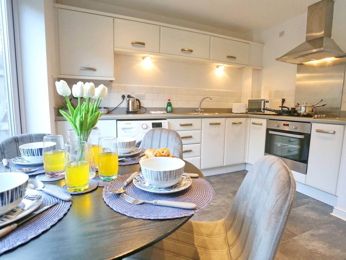 A modern kitchen with white cabinets, stainless steel appliances, and a dining area set for a meal.