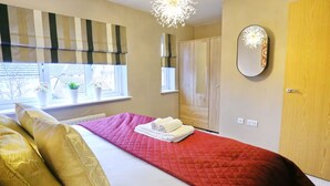 Un dormitorio con cama, mesita de noche, espejo, armario y ventana con cortinas.