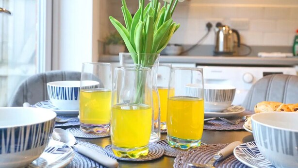 Una mesa de comedor con un jarrón de tulipanes blancos, tres vasos de líquido amarillo y varios cuencos y platos.