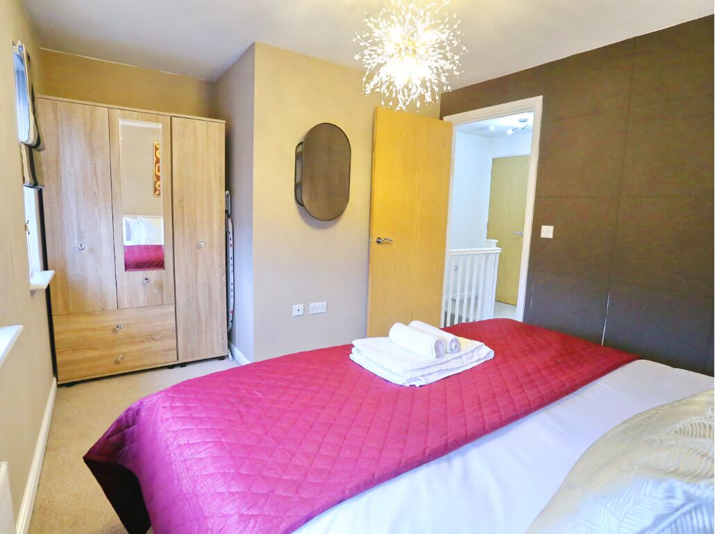 A bedroom with a bed, a wardrobe, a mirror, and a door leading to another room.