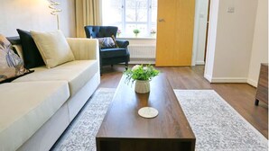 Una sala de estar con sofá, sillón, mesa de centro y ventana con cortinas.