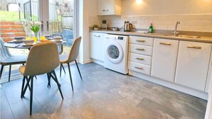 Una cocina moderna con lavadora integrada, un comedor con sillas y vistas al patio trasero a través de grandes ventanales.