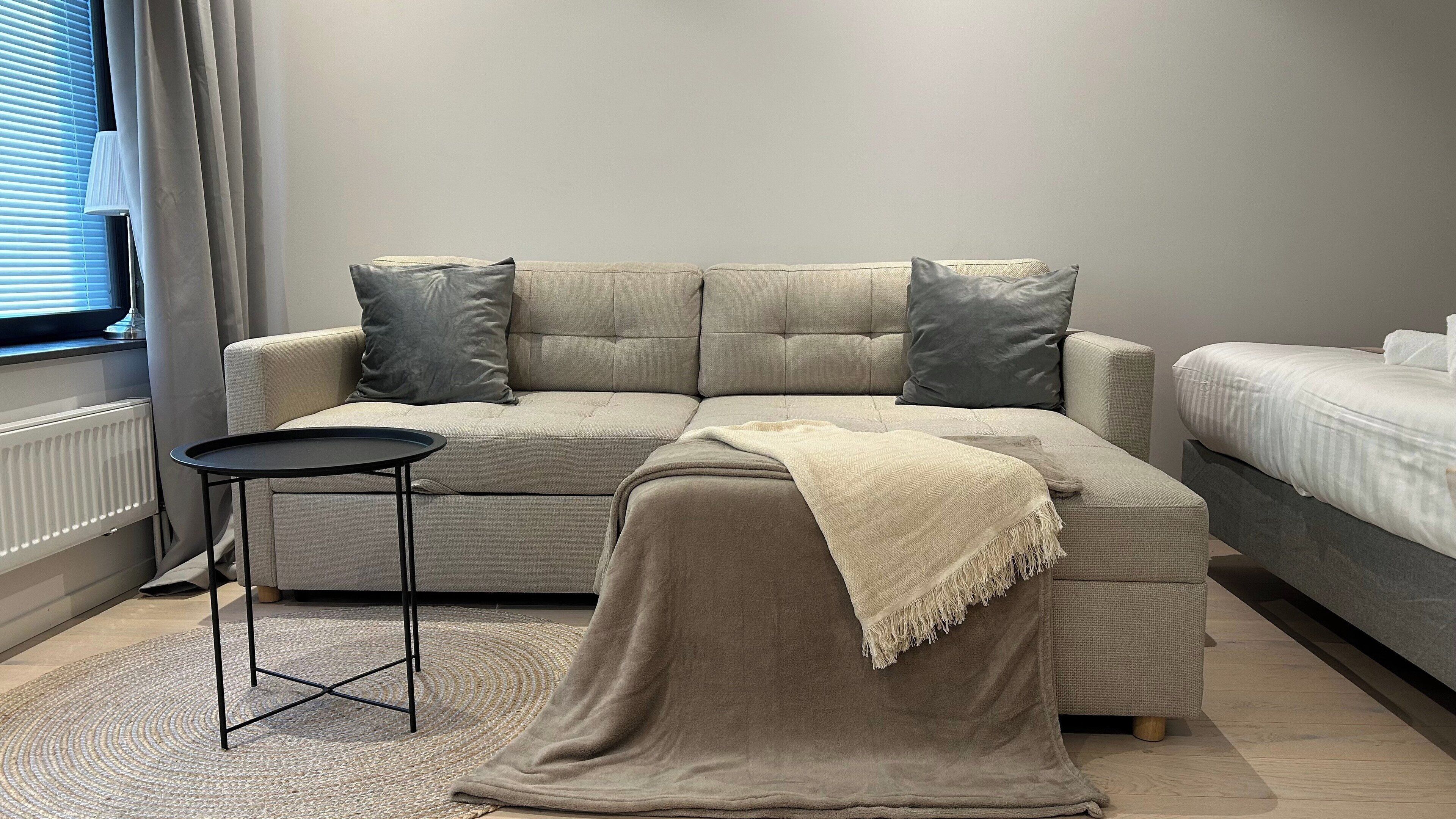Un salon moderne avec un canapé d’angle, une petite table d’appoint et un lit.