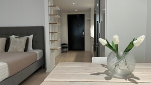 Un dormitorio moderno con una cama, una mesita de noche con un jarrón de flores blancas y un pasillo que conduce a una puerta oscura.