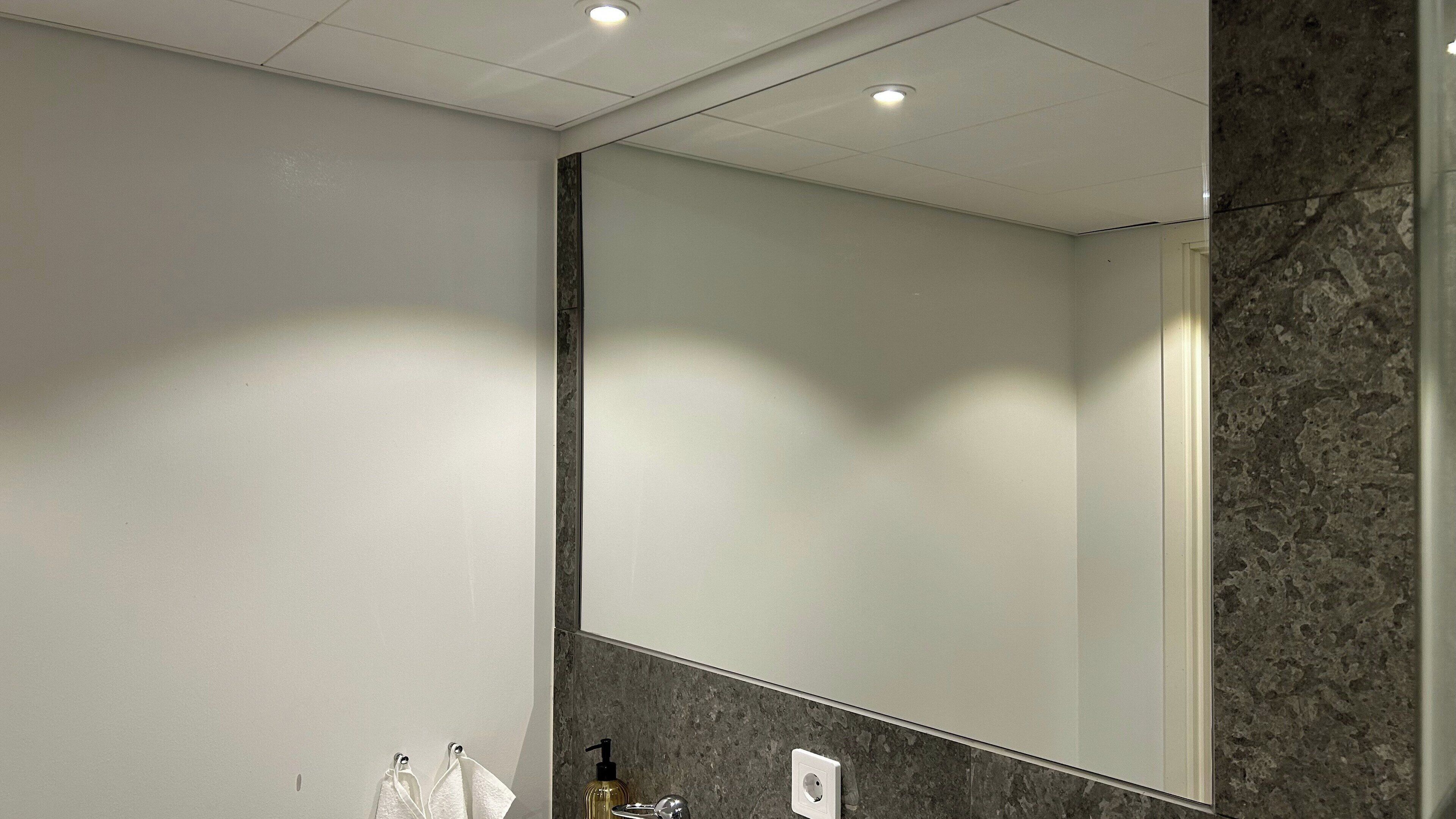 A bathroom with a large mirror, a marble countertop, and a wall-mounted soap dispenser.