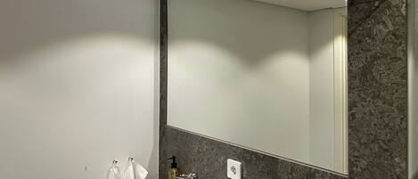 A bathroom with a large mirror, a marble countertop, and a wall-mounted soap dispenser.