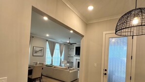 A modern living room with a sofa, a dining table, and a kitchen area with a TV and shelves. - Luxury and Executive 4-bedroom house, Close to Blue Oval City (Arlington)