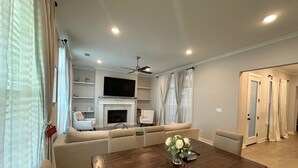 A modern living room with a fireplace, a flat-screen TV, and a dining area with a wooden table. - Luxury and Executive 4-bedroom house, Close to Blue Oval City (Arlington)
