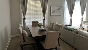 A modern living room with a dining area, featuring a large wooden table, beige sofas, and a large window with curtains. - Luxury and Executive 4-bedroom house, Close to Blue Oval City (Arlington)