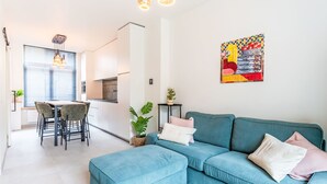 Een moderne woonkamer met een turquoise bank, een eethoek met een houten tafel en stoelen, en een keuken op de achtergrond.