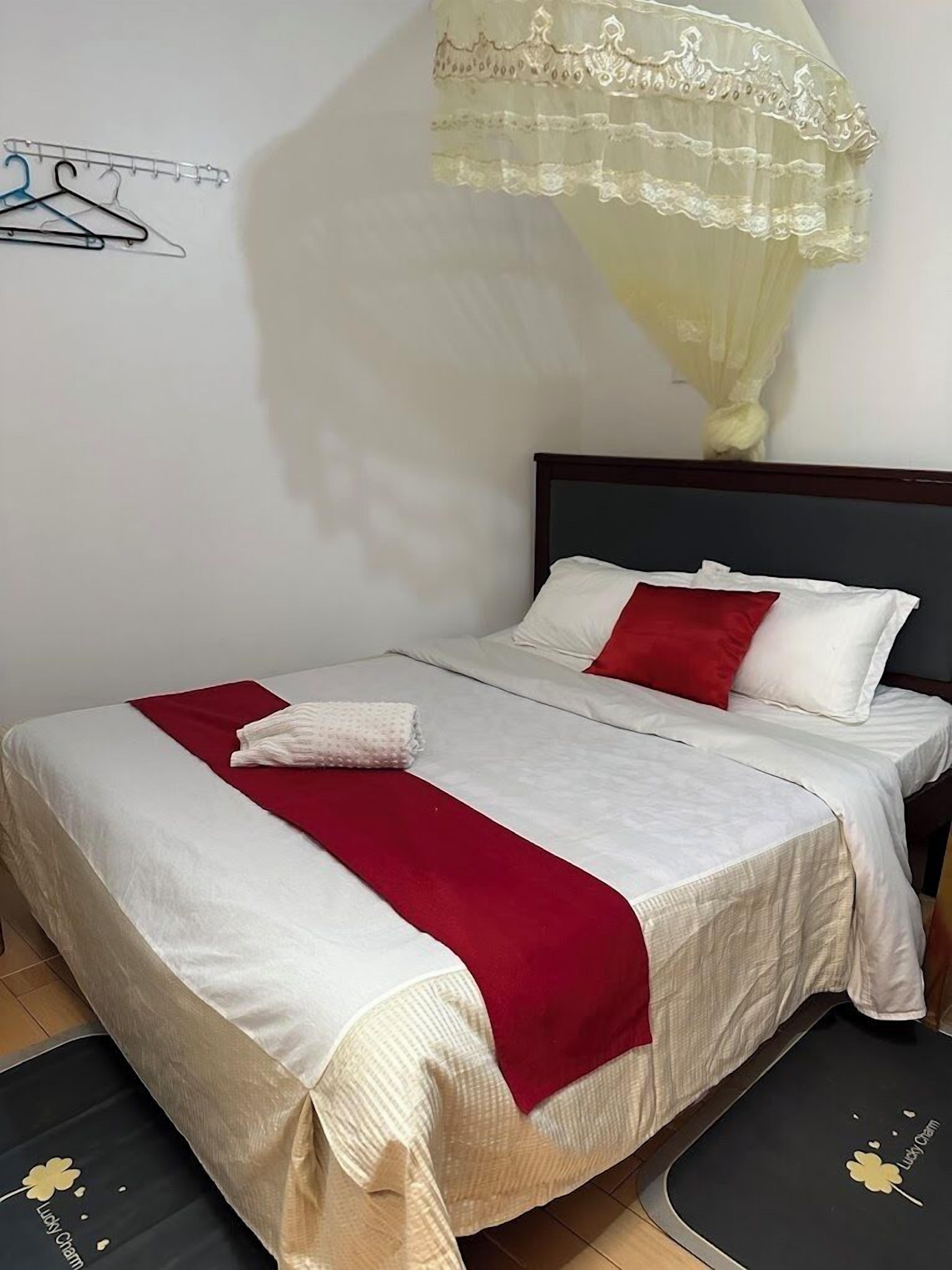 A neatly made bed with white and red bedding, a wooden headboard, and a wall-mounted coat rack with hangers.