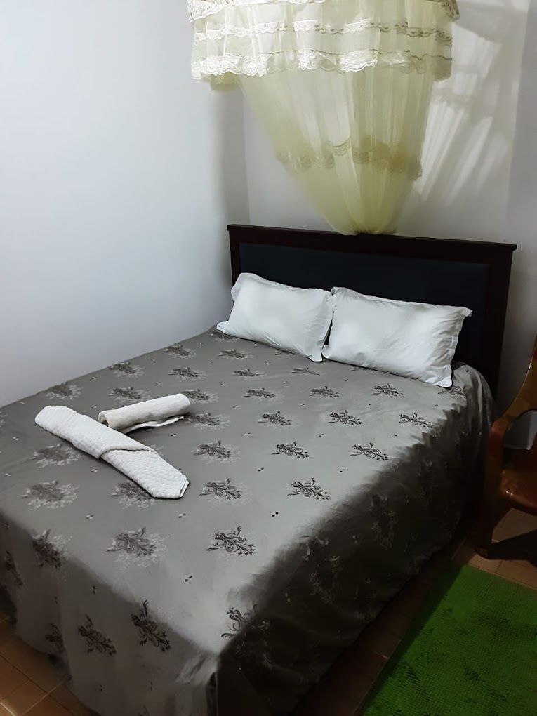 A single bed with a grey floral bedspread, two pillows, and a pair of folded towels.