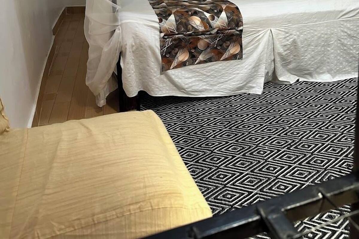 A bedroom with a canopy bed, a patterned bedspread, and a geometric-patterned rug.