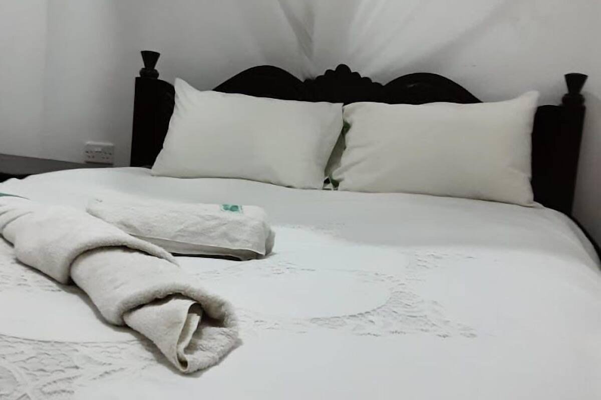 A neatly made bed with a white bedspread and pillows, a folded towel, and a dark wooden headboard.