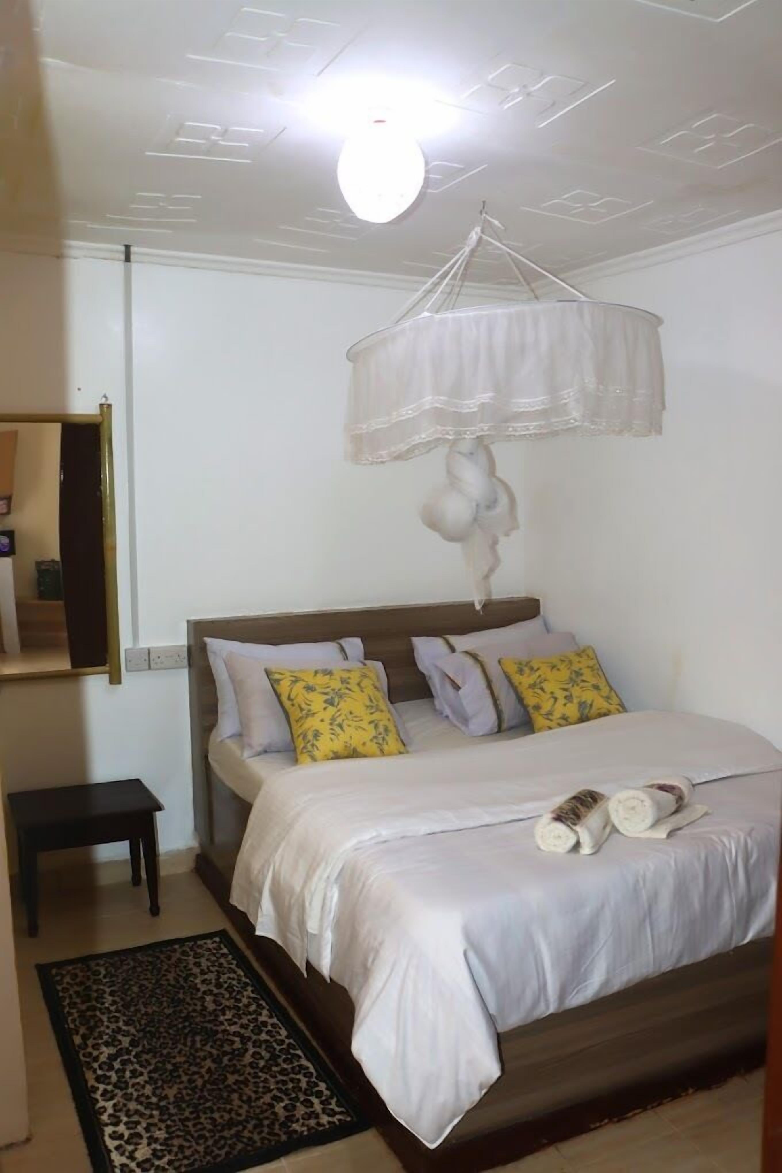 A bedroom with a bed, a hanging light fixture, a small table, and a leopard print rug.
