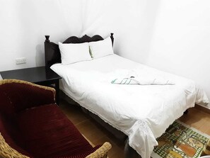 A single bed with white linens, a dark wooden headboard, and a small bedside table.