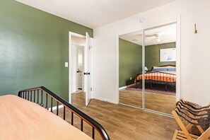 Une pièce avec un lit, un plancher en bois, un mur vert et une porte coulissante donnant sur une autre pièce.