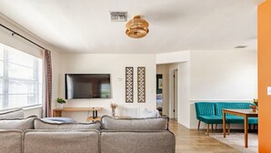 A living room with a sofa set, a television, and a dining area with a table and chairs. - Updated 2 BR / 5 min to Advent Health / Walk to Museums, Parks & Dining. (Orlando)
