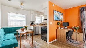 A modern living space with a teal sofa, a wooden dining table, a kitchen area, and a workspace with a desk and chair. - Updated 2 BR / 5 min to Advent Health / Walk to Museums, Parks & Dining. (Orlando)