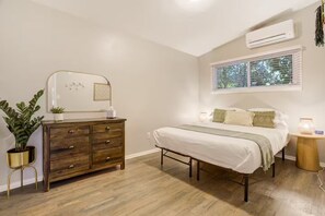 Un dormitorio con cama, cómoda, mesita de noche, ventana y aire acondicionado.