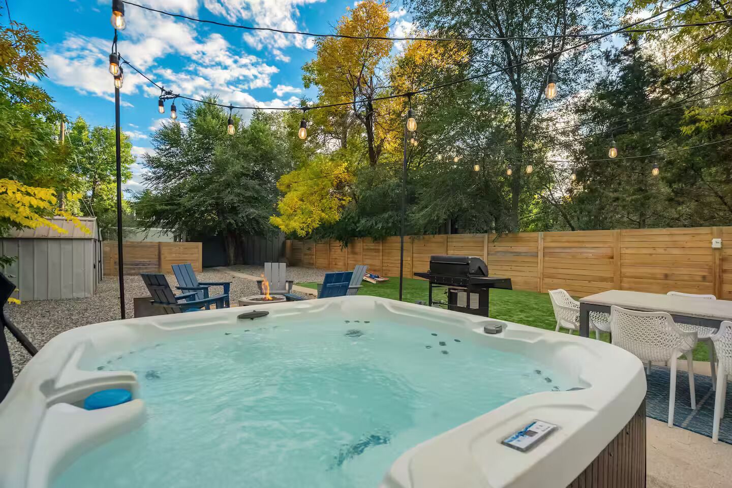 A backyard with a hot tub, outdoor seating, and a wooden fence.