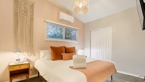 A bedroom with a bed, bedside table, lamp, air conditioning unit, window with blinds, and a door. - Pet-friendly Getaway near Cheyenne Cañon&Ivy wild (Colorado Springs)