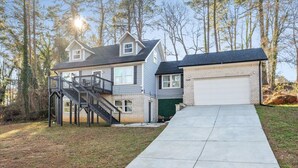 Een huis met twee verdiepingen, een garage, een overdekte veranda en een oprit van beton.