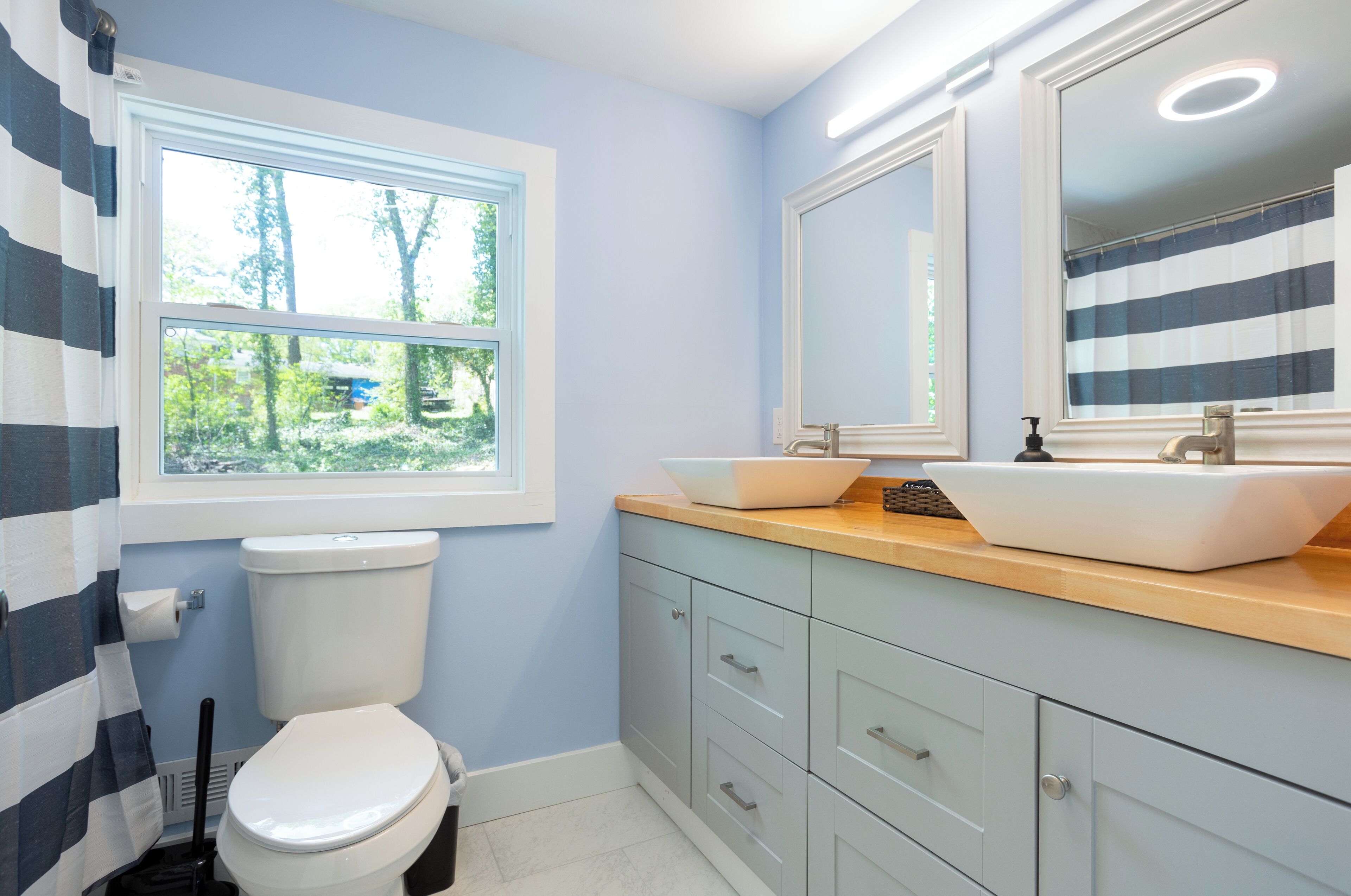 Une salle de bain avec une fenêtre, des toilettes, un lavabo et des placards.