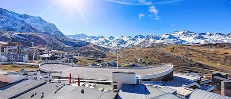 A modern building with a curved roof, surrounded by snow-capped mountains and clear blue skies.