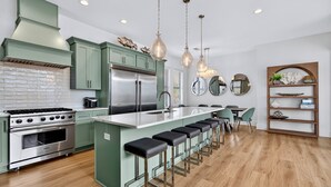 A modern kitchen with green cabinets, stainless steel appliances, and a central island with bar stools. - Arcadia Sands: Private Beach, Ocean Views, Pool & Hot tub, Game Room, Bunk Rooms (Miramar Beach)