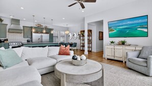 A modern living room with a sectional sofa, a round coffee table, and a dining area with a table and chairs. - Arcadia Sands: Private Beach, Ocean Views, Pool & Hot tub, Game Room, Bunk Rooms (Miramar Beach)