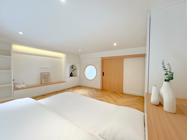 Un dormitorio moderno con una cama grande, un espejo redondo, un armario de madera y una pequeña estantería con un florero.