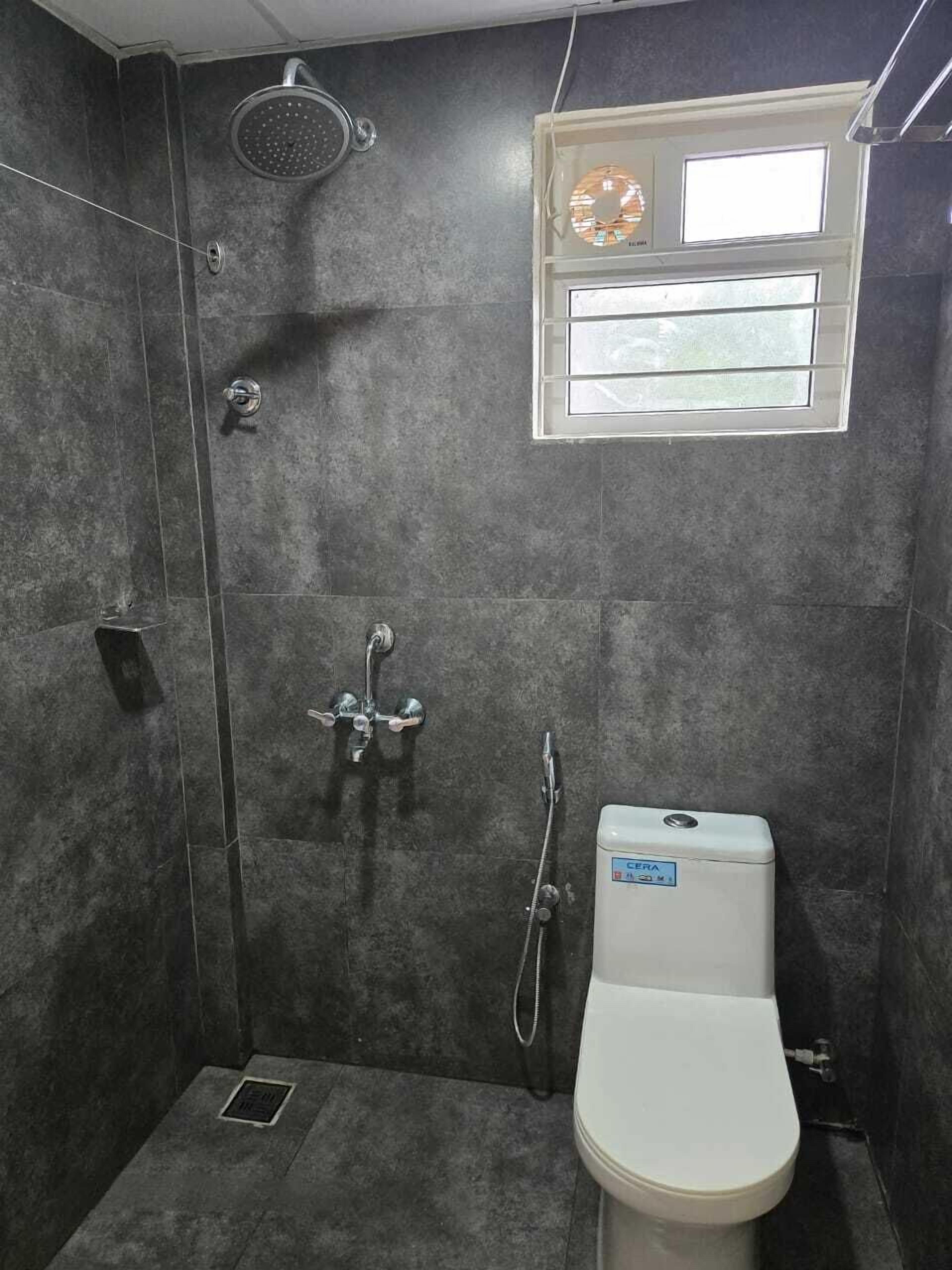 A compact bathroom with a shower, toilet, and a small window.