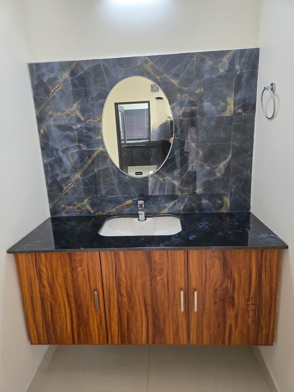 A bathroom with a marble backsplash, a round mirror, a sink, and wooden cabinets.