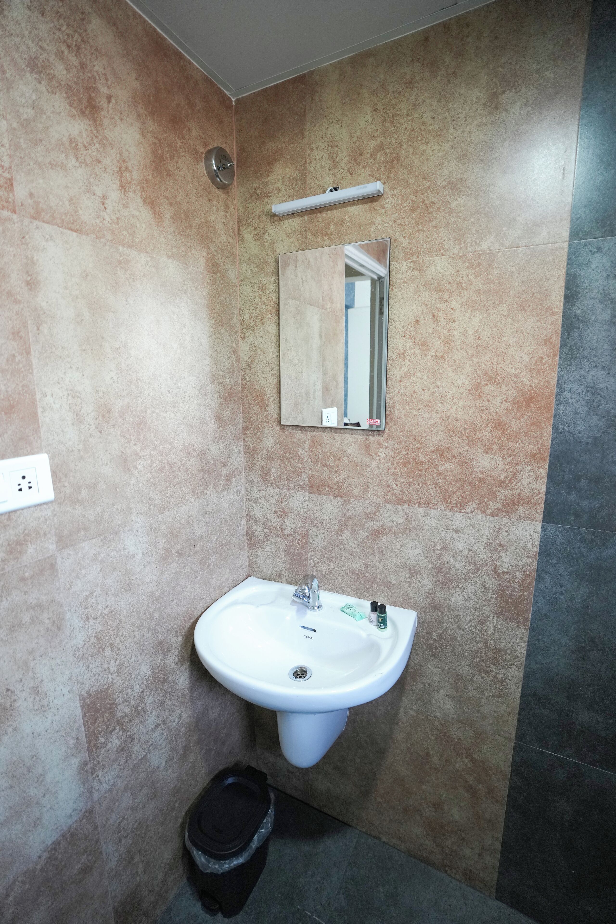 Een badkamer met een witte wasbak, een spiegel en een prullenbak.