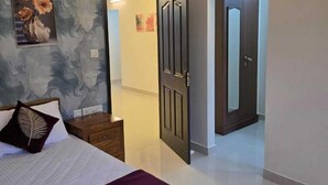 Une chambre à coucher comprenant un lit, une table de chevet, une commode, un ventilateur de plafond et une porte donnant sur une autre pièce.