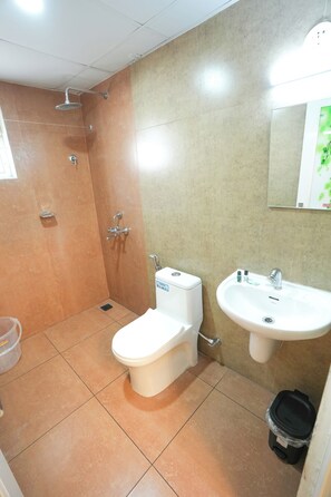 A bathroom with a shower, toilet, sink, and a trash bin. - Centur Apartments (Changanassery)