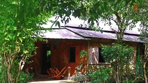 A rustic wooden house with a corrugated metal roof, surrounded by lush greenery and a well-maintained garden. - Swiss Valley Resort (Kamalganj)